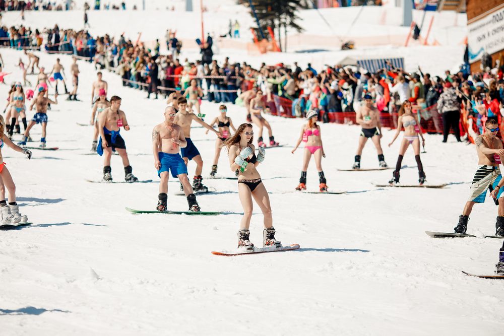 People in swimsuits and bathing suits go down a winter slope during Grelka fest
