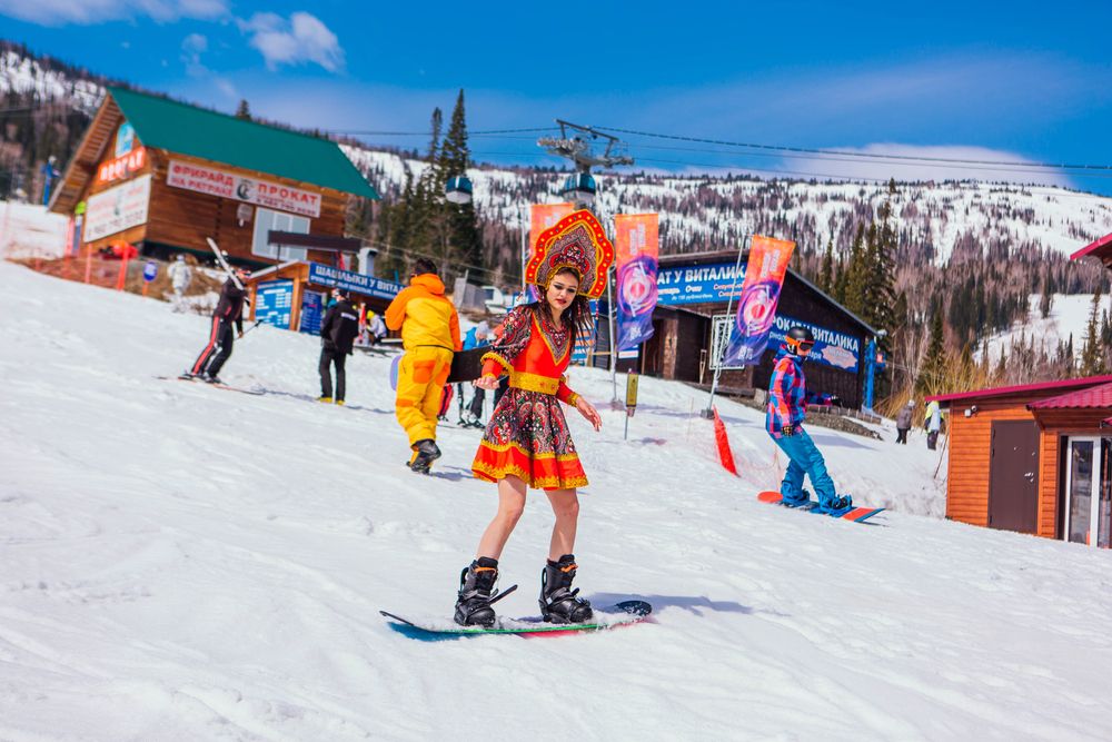 Girl in Russian folk costume goes downhill on a snowboard in Sheregesh